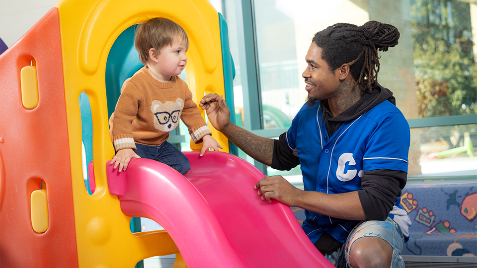 child on slide and MATC childcare worker